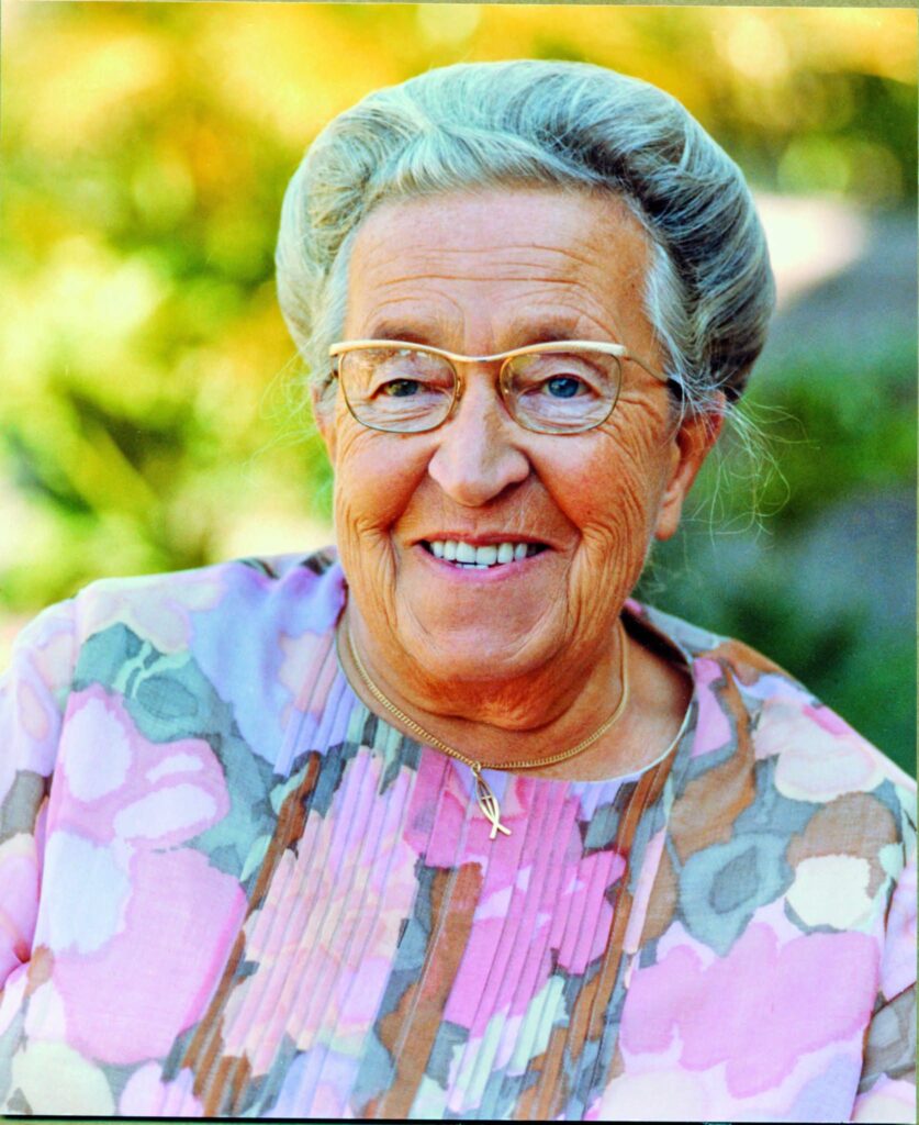 Smiling elderly woman outdoors wearing glasses and a floral top."
